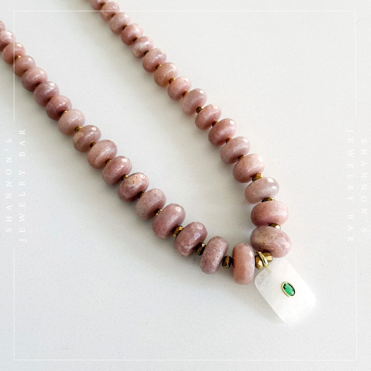 A beaded necklace with dusty pink stone beads, small gold spacer beads, and a white rectangular pendant featuring a green inlay, displayed on a light gray background.  Peach Moonstone, Faceted Graduated Beads.