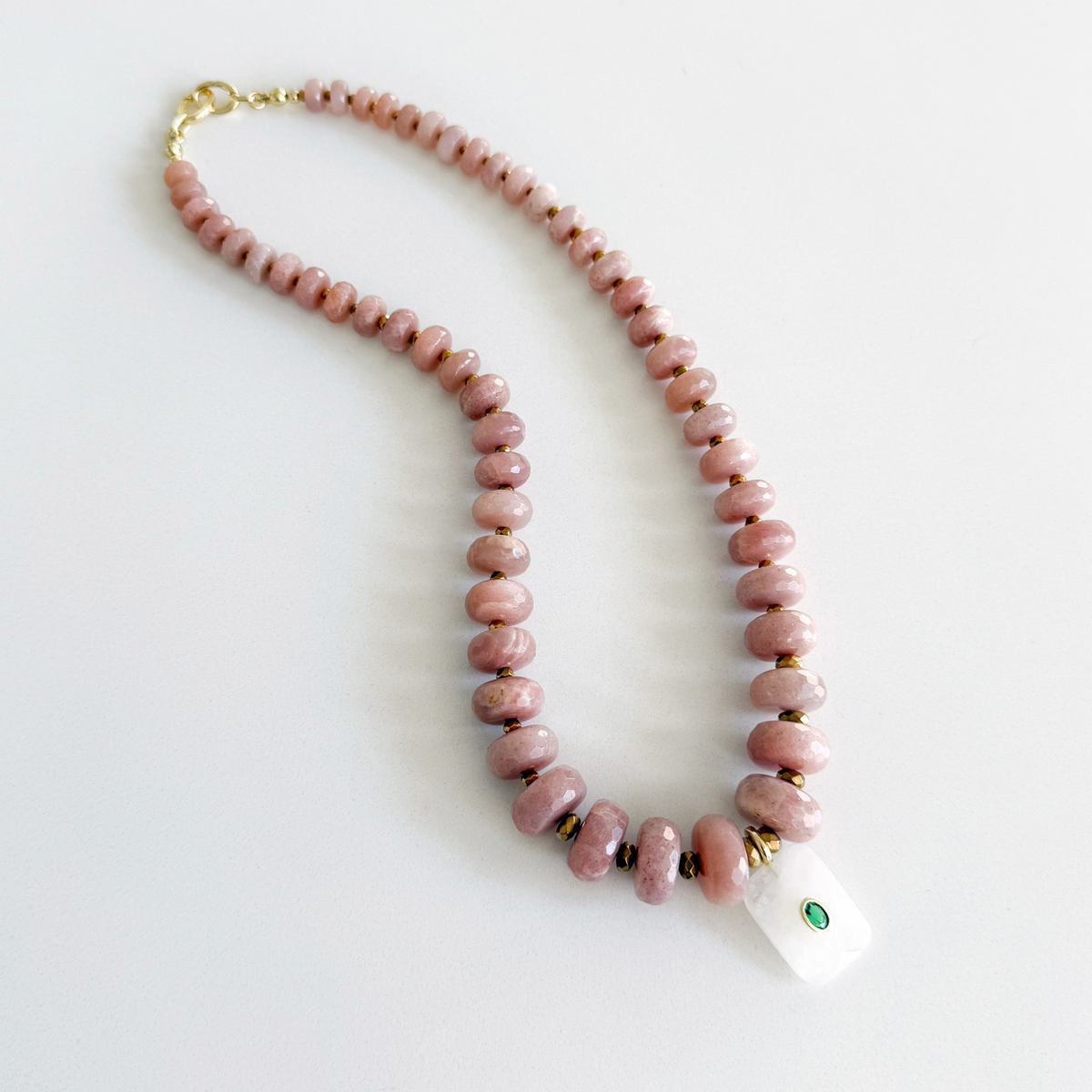 A pink stone bead necklace with a white rectangular pendant featuring a small green stone, displayed on a clean white background. Peach Moonstone, Faceted Graduated Beads.